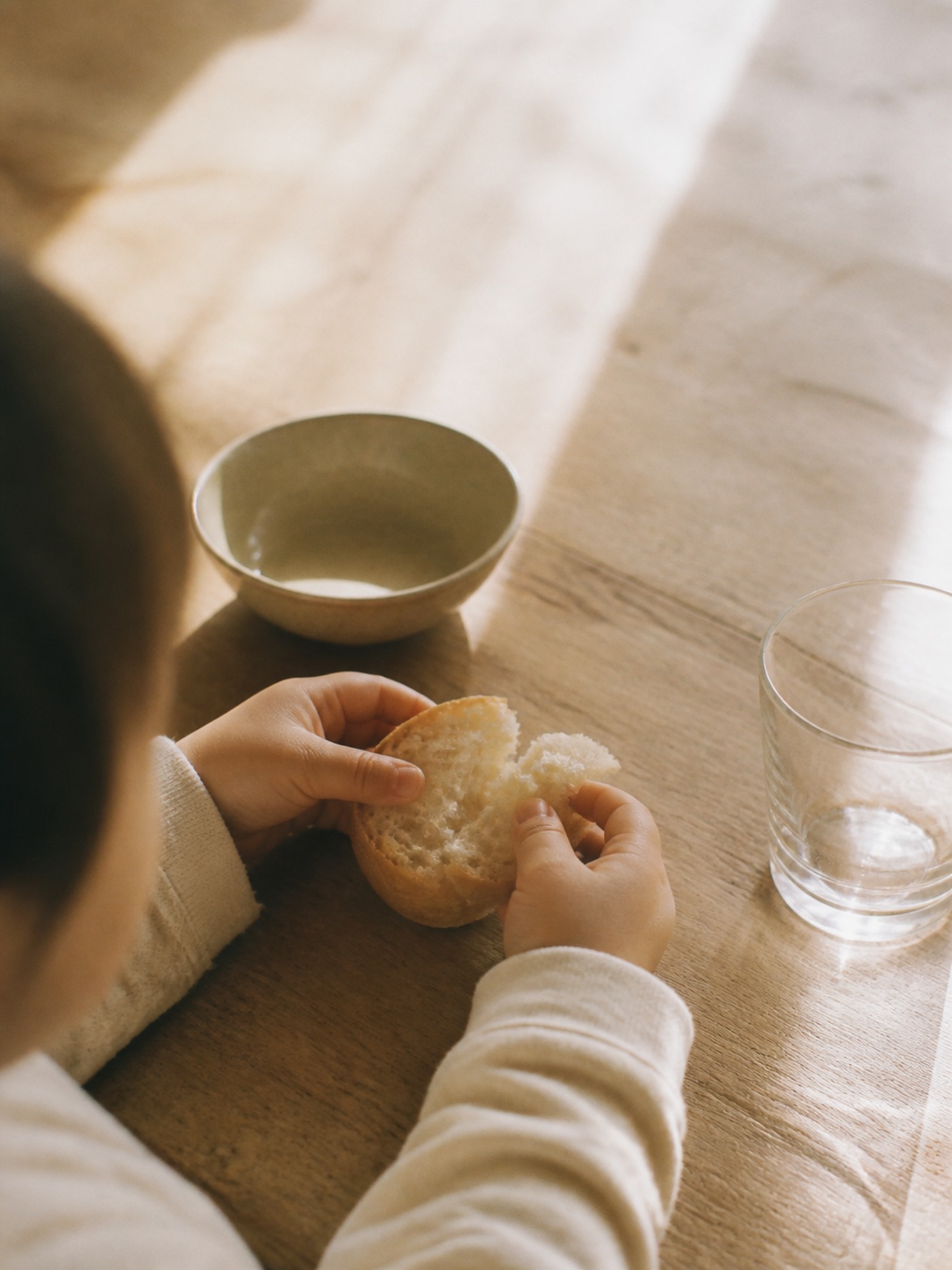 朝日の当たるテーブルでパンをちぎる子どもの手